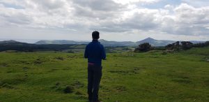 A person standing with his back to us looking at a landscape of grassy fields