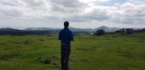 A person standing with his back to us looking at a landscape of grassy fields